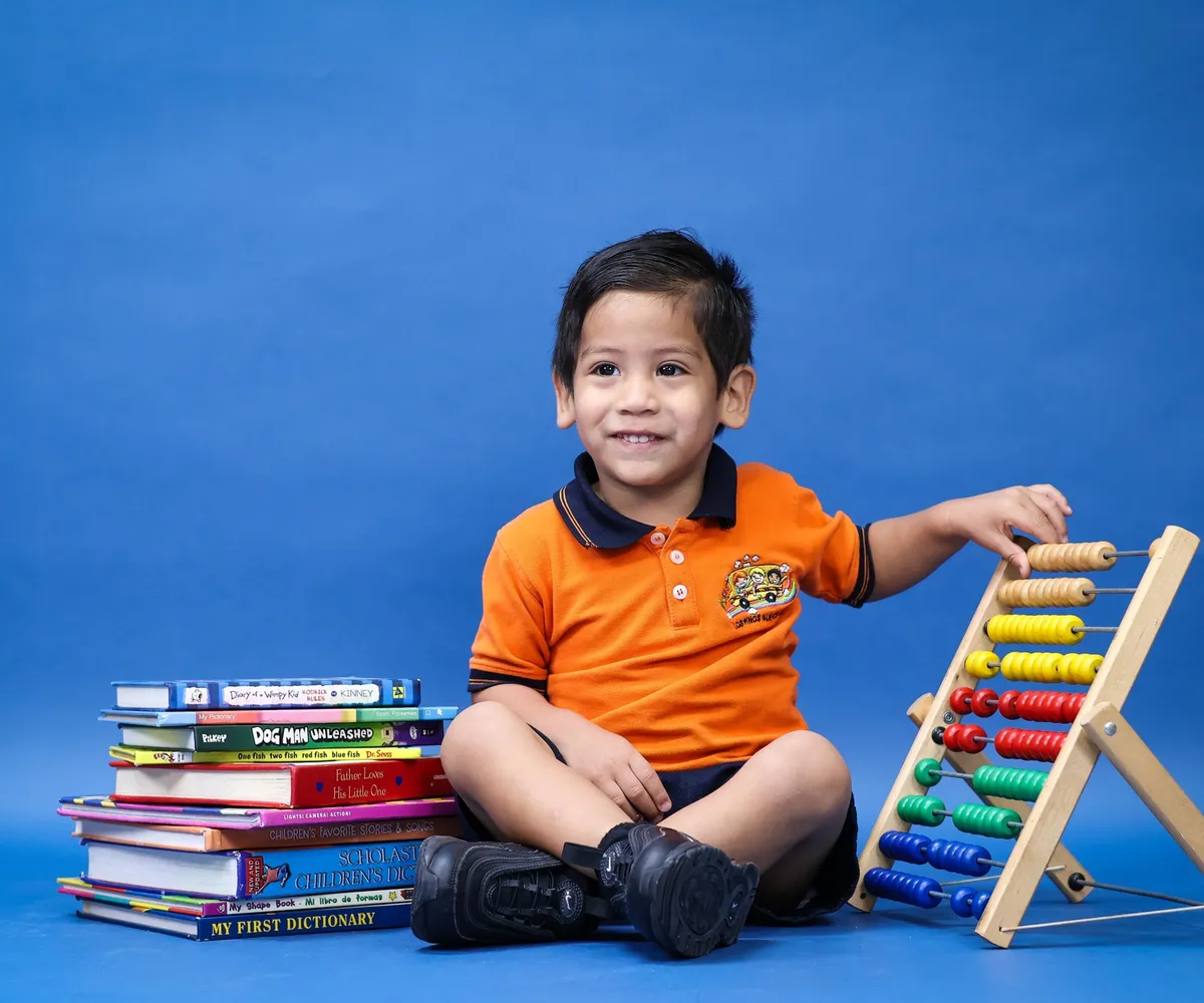 Niño de tres añitos sentado en el piso, jugando con un ábaco de colores junto a su pila de libros