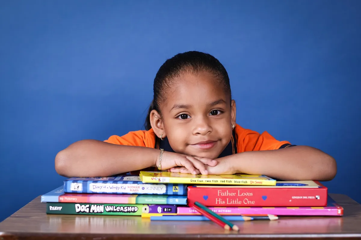 Estudiante de kindergarten apoyando la barbilla sobre sus libros favoritos, sonriendo