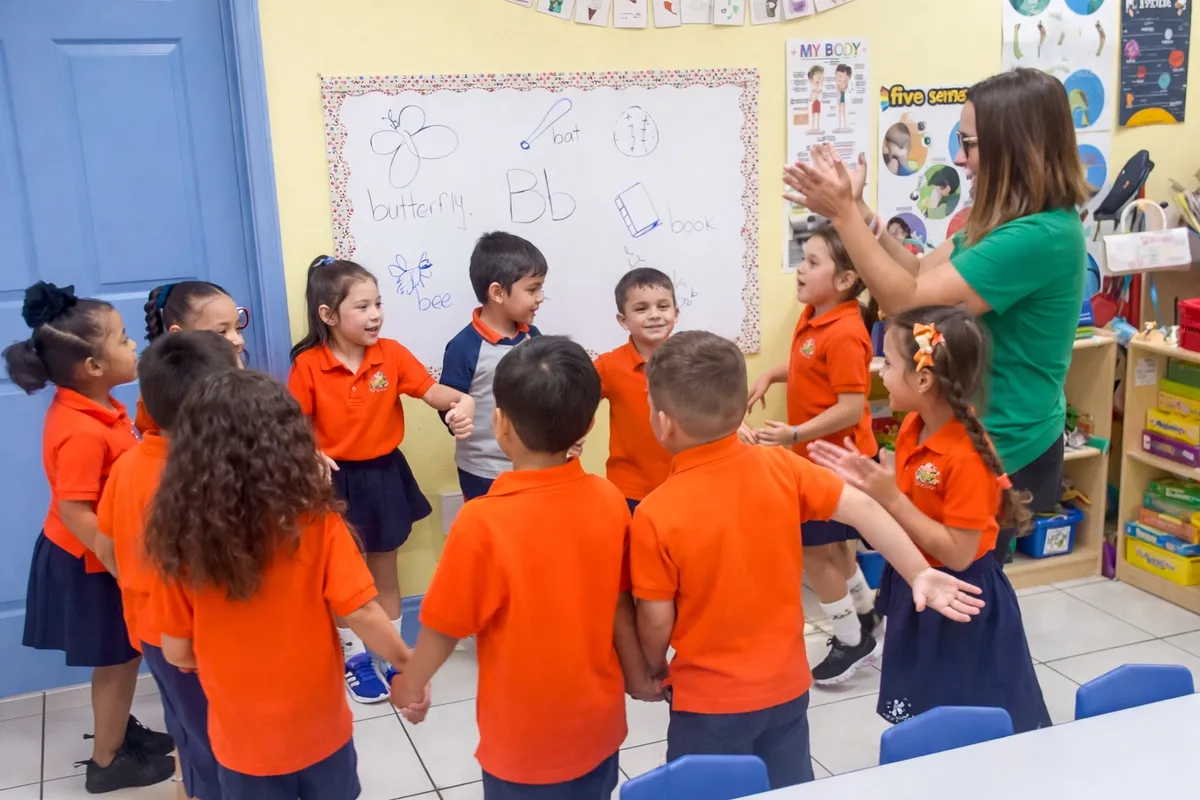 Clase de VPK tomada de las manos en círculo con su maestra, aprendiendo la letra B